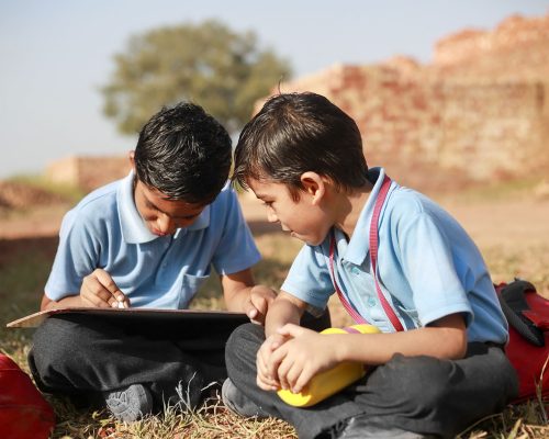 Elementary students of Indian ethnicity sitting together outdoor and studying portrait close up during summer season.